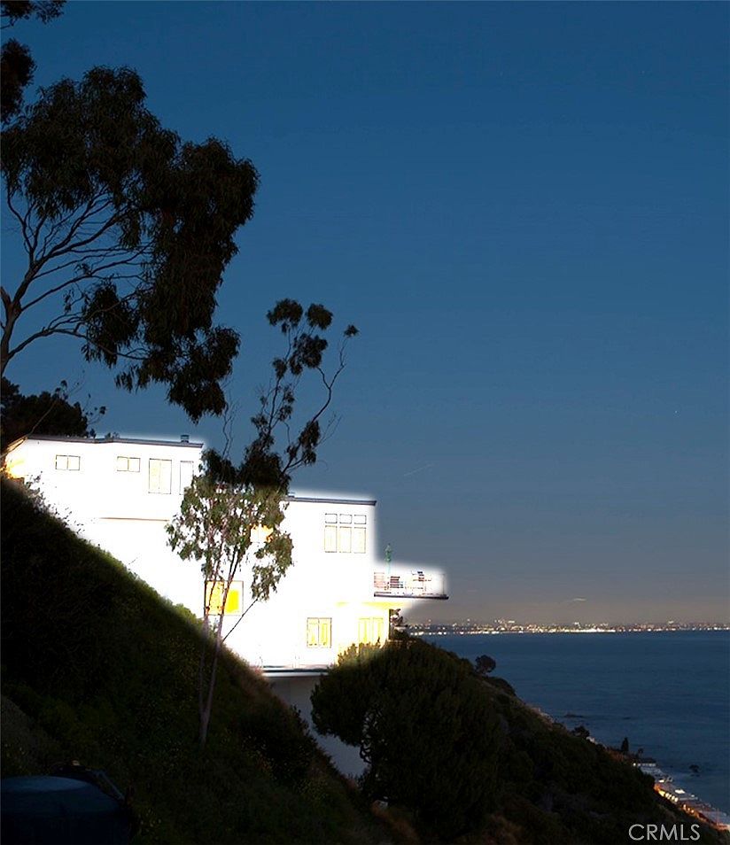 Twilight view of a neighboring Malibu home perched on the cliffside, showing the city lights across the bay.